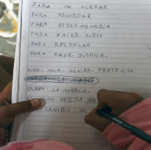 Fotografía de un cuaderno, sostenido por una niña o niño que está escribiendo las frases: Para no olvidar, para recordar, para dejar memoria, para hacer duelo, para rectificar, para hacer justicia, uno- nua- olvida- presente, queda –la - marca, es como herida.